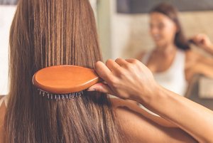 Brunette woman brushing her hair with a wooden hairbrush with rounded bristles